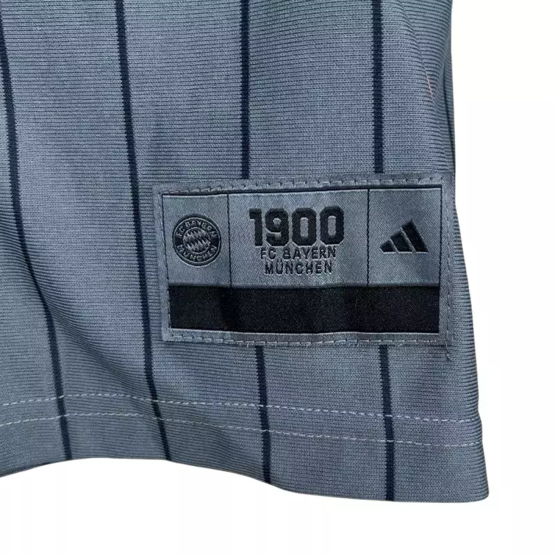 Jersey close up showing Bayern Munich special edition shirt 2025 hem patch with 1900 crest and Adidas logo on pinstripe fabric