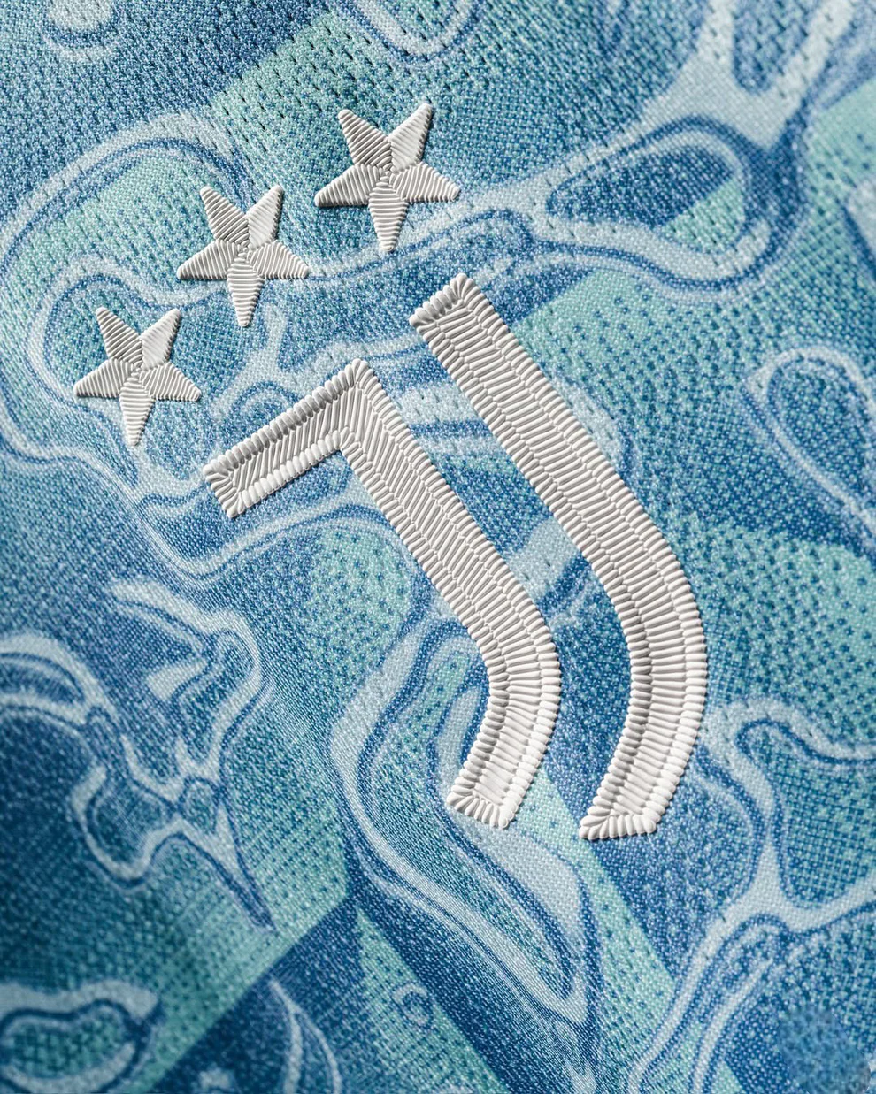 Close-up of blue patterned fabric with embroidered Juventus logo and three stars on Juventus away jersey 25-26