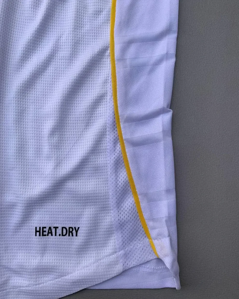 Hoop Store close up of Real Madrid 2025 home jersey white mesh with yellow side piping and HEAT DRY branding