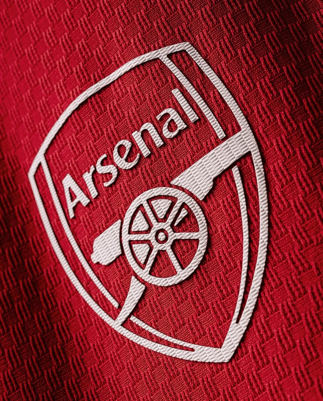 Close-up of the Arsenal Home Jersey 2026-27 logo with detailed embroidery on a red fabric background