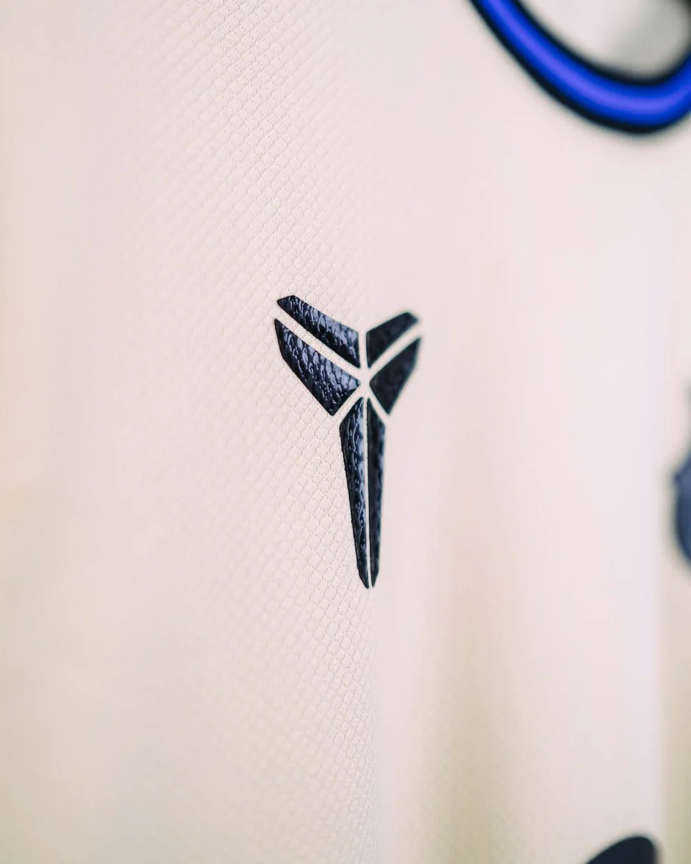 Hoop Store Barcelona away jersey 2025-26 close up of textured black emblem on cream fabric with blue trim