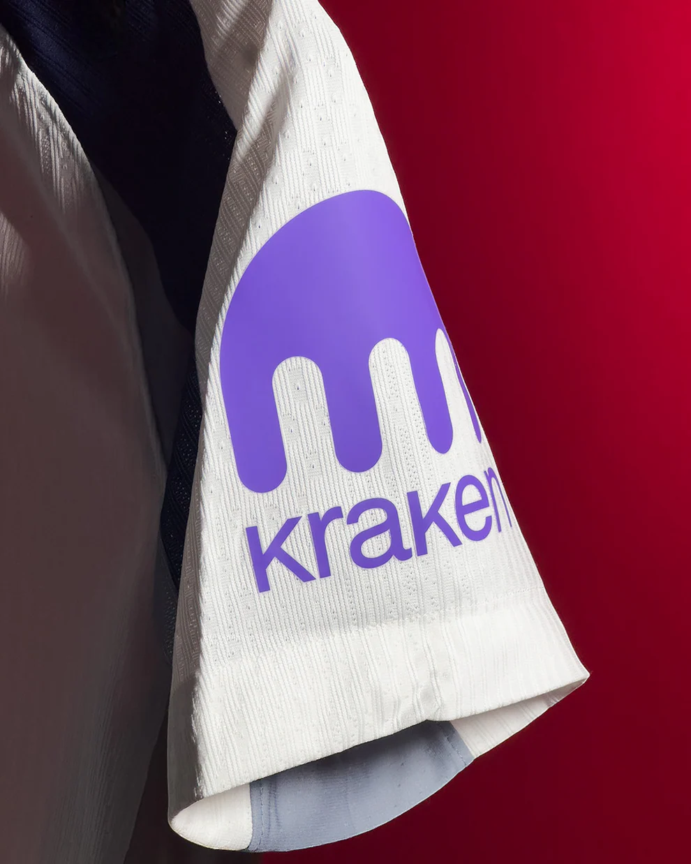 Close up of white Tottenham Hotspur 2025 home jersey sleeve with purple Kraken sponsor logo on textured fabric